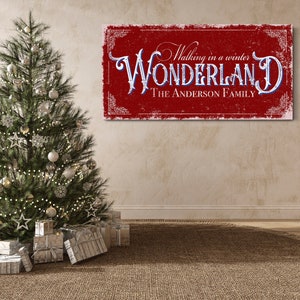 May include: Red and white sign with the text "Walking in a winter WONDERLAND THE ANDERSON FAMILY" in a vintage style font. The sign is hanging on a beige wall with a Christmas tree in the foreground.
