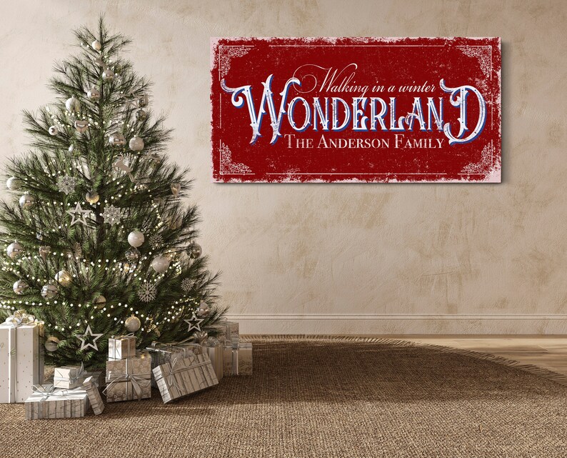 May include: Red and white sign with the text "Walking in a winter WONDERLAND THE ANDERSON FAMILY" in a vintage style font. The sign is hanging on a beige wall with a Christmas tree in the foreground.