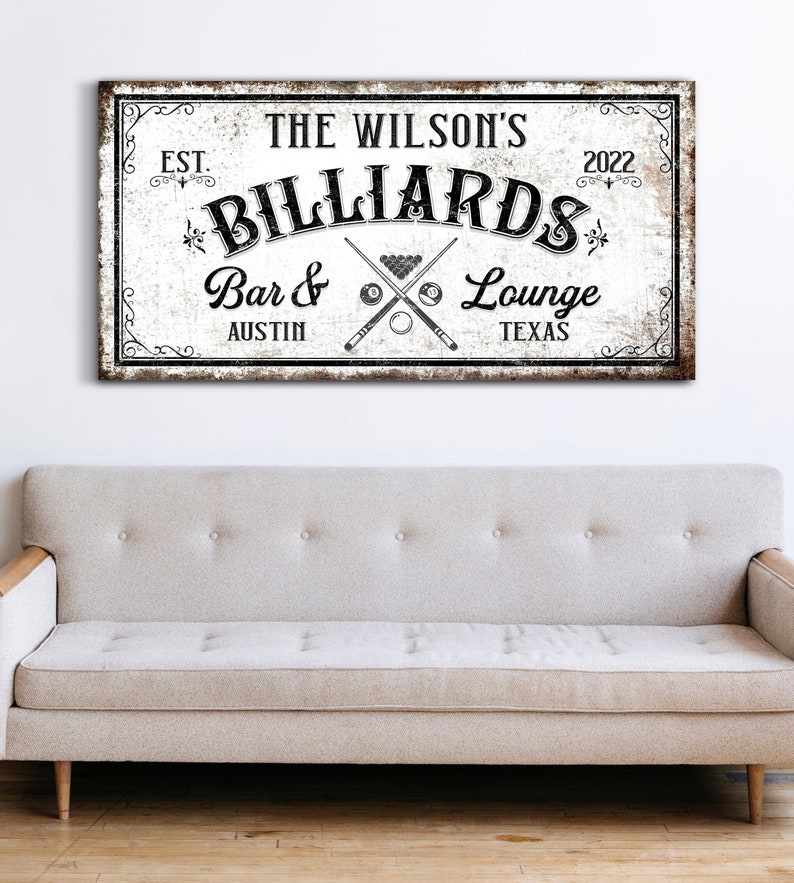 May include: A vintage-style sign with the text "The Wilson's Billiards Bar & Lounge Austin Texas Est. 2022" in black lettering on a white background. The sign has a distressed, weathered look and features a crossed pool cue and billiard balls.