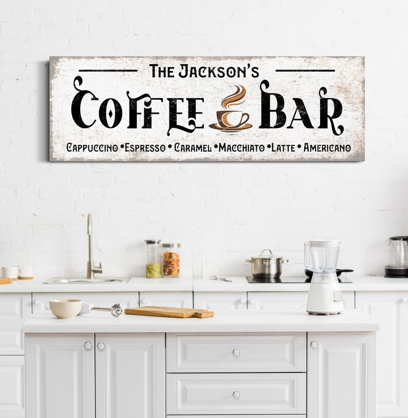 May include: A white wooden sign with black text that reads "The Jackson's Coffee & Bar" with a brown coffee cup icon and the text "Cappuccino, Espresso, Caramel, Macchiato, Latte, Americano" underneath.