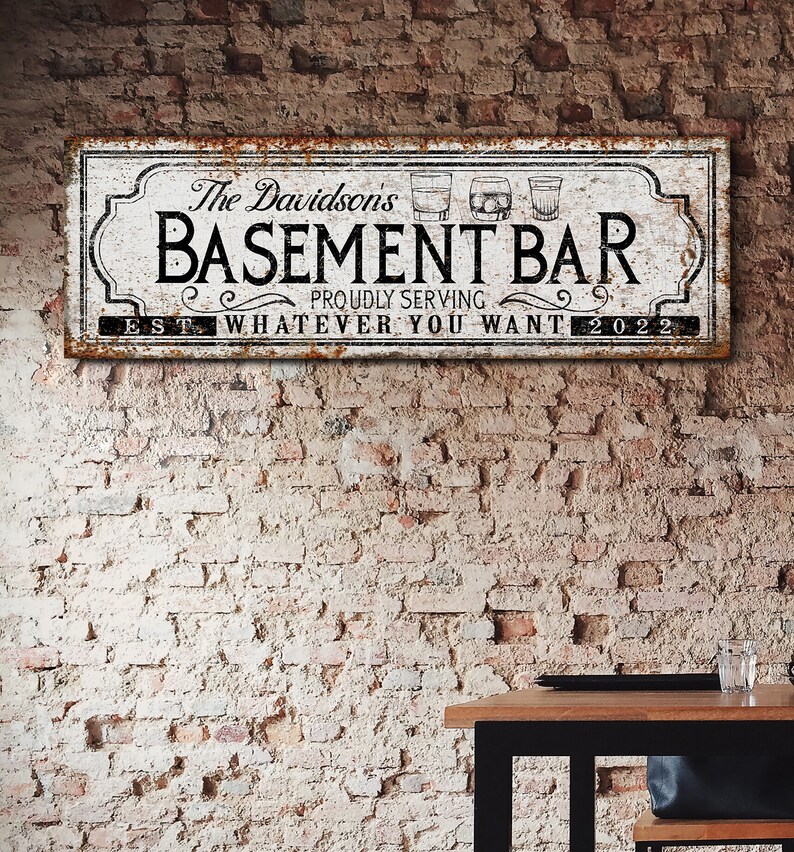 May include: A white sign with black text and a rusty border reads "The Davidson's Basement Bar Proudly Serving Whatever You Want Est 2022". Three white silhouettes of glasses are above the word "Bar".