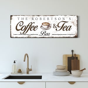 May include: A rectangular wooden sign with the text "THE ROBERTSON'S Coffee & Tea Bar" in brown and black lettering. The sign features a coffee cup illustration and a distressed white background.