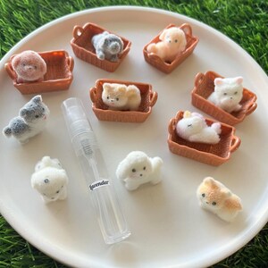 Puede incluir: Una colecci&oacute;n de figuras de animales de peluche en miniatura, incluyendo perros y un unicornio, metidas en peque&ntilde;as cestas marrones. Tambi&eacute;n hay un frasco de spray transparente etiquetado "lavender", todo dispuesto sobre un plato blanco.