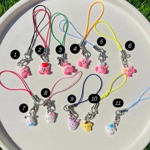 May include: Eleven colourful phone charms with pink, yellow, and white characters attached. The charms are numbered 1 through 11.