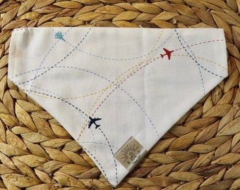 Peut inclure: Bandana en coton blanc avec un motif d'avion bleu, rouge et jaune. La bandana a un motif cousu de lignes et de courbes. La bandana a une petite étiquette blanche avec un soleil et un oiseau.