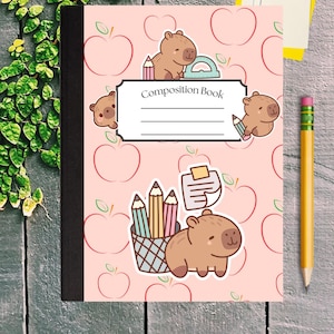 May include: A composition book with a light pink cover featuring a repeating apple pattern and cartoon capybaras. The center label reads Composition Book with lines for writing. Illustrations include capybaras with pencils, a protractor, and a pencil holder.
