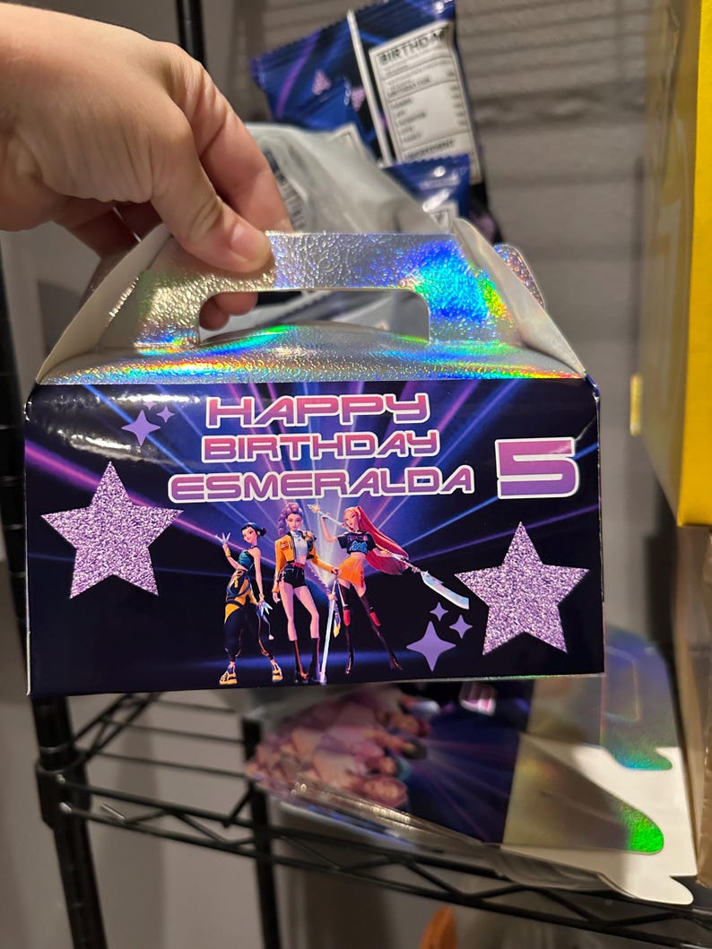 May include: A holographic birthday gift box with the text "HAPPY BIRTHDAY ESMERALDA 5". The box features a design with three figures, purple stars, and a holographic handle.