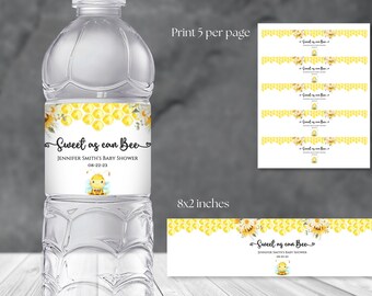 May include: Water bottle label template with a bee and honeycomb design. The label says "Sweet as can Bee" and includes the text "Jennifer Smith's Baby Shower" and the date "08-22-23". The template is 8 inches by 2 inches and can be printed 5 per page.