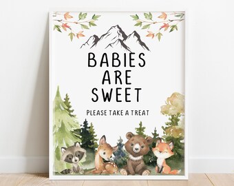 May include: A framed print with the text "BABIES ARE SWEET PLEASE TAKE A TREAT" above watercolor illustrations of mountains, trees, and woodland animals. The animals include a raccoon, deer, bear, and fox. The print has a white border.