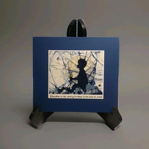 May include: A framed artwork featuring a silhouette of a child seated, with a textured background in shades of blue and white. The artwork is displayed on a dark blue square card, with the text "Education is like carving on stone-it can never be erased".