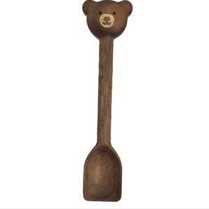 May include: A wooden spoon with a brown bear face carved on the handle. The spoon is dark brown and has a rounded scoop.