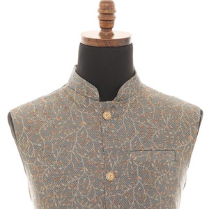 May include: A gray sleeveless vest with a gold floral pattern and gold buttons. The vest has a mandarin collar and two pockets.