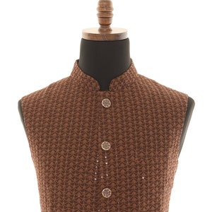May include: A brown, sleeveless vest with a mandarin collar, displayed on a mannequin. The vest features a repeating geometric pattern and is fastened with decorative buttons. The garment is a formal wear item.