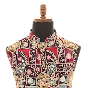 May include: A sleeveless vest with a maroon background and intricate embroidery in shades of red, gold, pink, and blue. The embroidery features floral patterns, paisley designs, and geometric shapes.