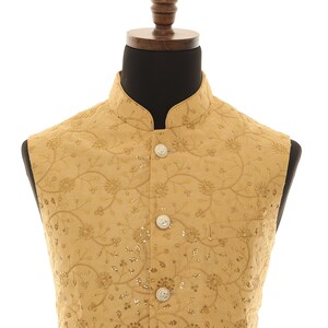 May include: A gold sleeveless vest with a floral pattern and button closure.