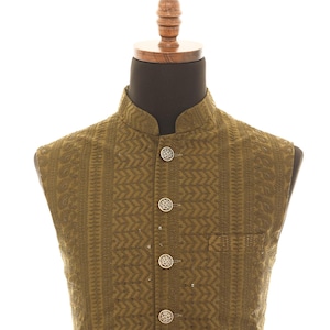 May include: A sleeveless olive green vest with a mandarin collar and a button-up front. The vest has a geometric pattern and silver buttons.