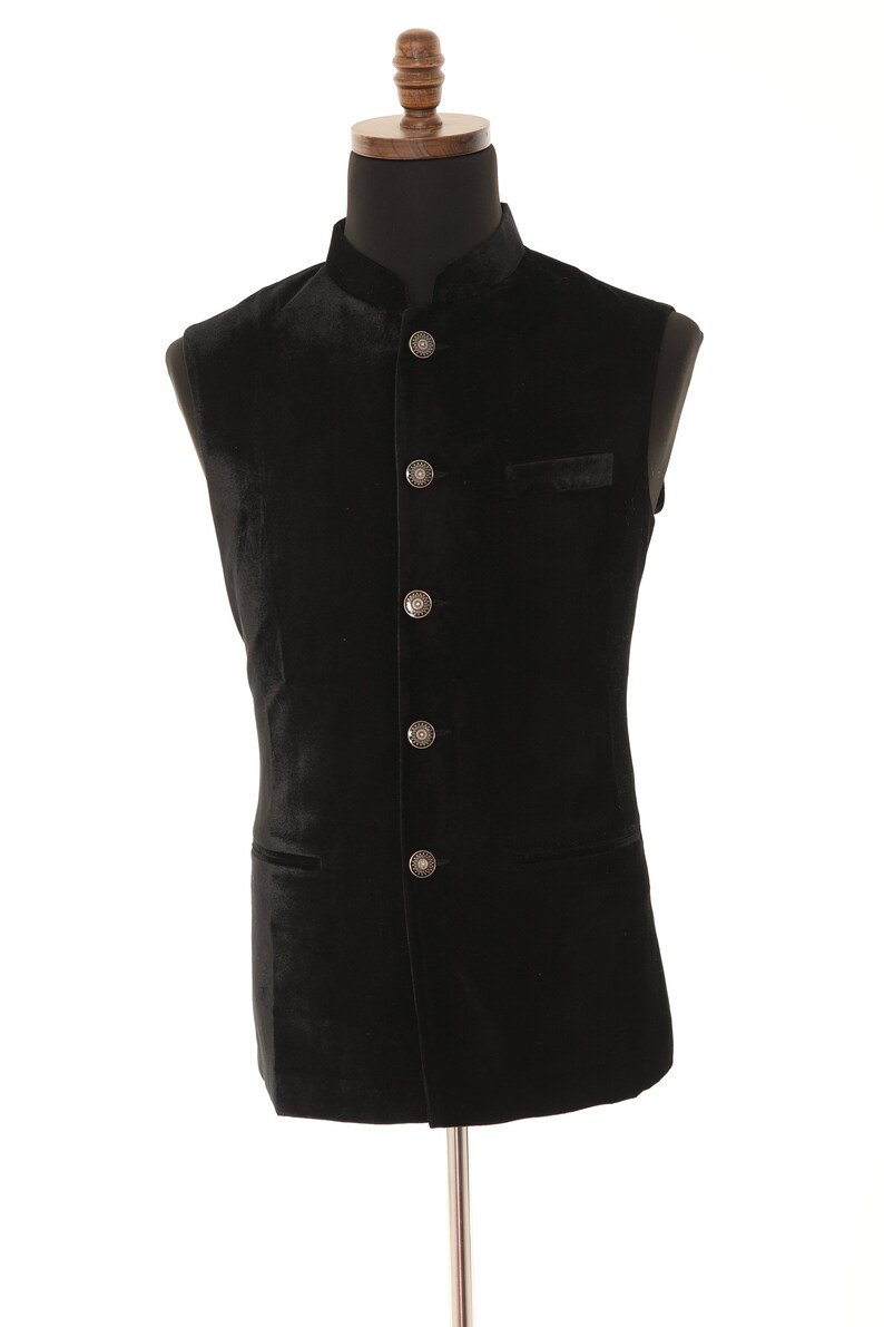 May include: A black velvet waistcoat with a mandarin collar and silver buttons. The waistcoat has two pockets and is sleeveless.