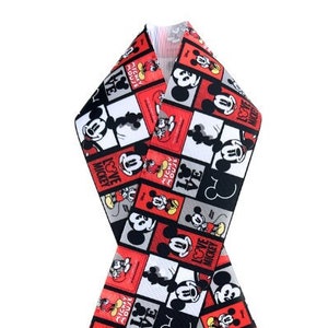 May include: A decorative scarf featuring a repeating pattern of Mickey Mouse in red, black, white, and gray squares. The scarf is folded in a figure-eight shape, showcasing the design.