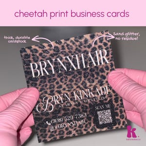 Peut inclure: Une carte de visite rectangulaire avec un motif imprimé guépard noir et marron et une texture scintillante. La carte présente le texte blanc BRYNXHAIR, BRYN KINKADE KEARNEY HAIRSTYLIST, un numéro de téléphone, un compte Instagram et un QR code.