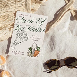 May include: A white card with black calligraphy that reads "Abigail's Fresh Off The Market" and a line drawing of a bouquet of flowers and a mesh bag with produce. The card also includes the text "Join us for a Bachelorette Weekend" and "June 5th - June 8th, San Diego, California".