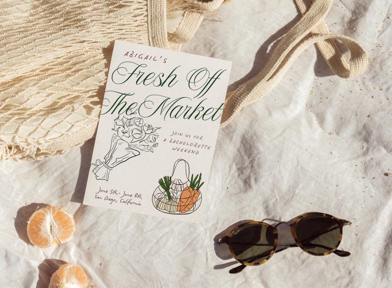 May include: A white card with black calligraphy that reads "Abigail's Fresh Off The Market" and a line drawing of a bouquet of flowers and a mesh bag with produce. The card also includes the text "Join us for a Bachelorette Weekend" and "June 5th - June 8th, San Diego, California".