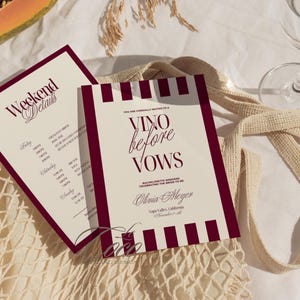 Op de afbeelding: Twee crèmekleurige uitnodigingskaarten met bordeauxrode accenten. Eén kaart leest "Weekend Details" en de andere zegt "Vino before Vows" voor een vrijgezellenweekend in Napa Valley. De kaarten liggen op een crèmekleurige nettas.