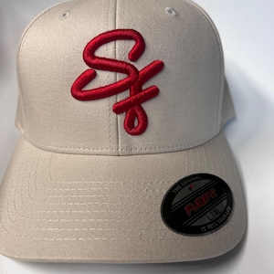 May include: A beige baseball cap with a red embroidered "SF" logo on the front. The cap has a black Flexfit label on the back with the text "The Original Flexfit L/XL It Fits Your Life."