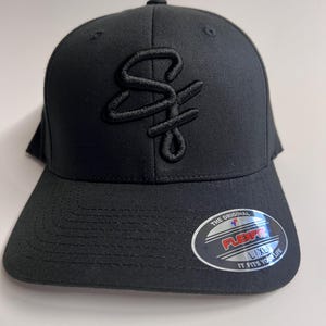 May include: Black baseball cap with a black embroidered logo that says "SF". The cap has a black Flexfit label on the back that says "The Original Flexfit L/XL It Fits Your Life".
