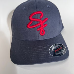 May include: A dark blue baseball cap with a red embroidered "SF" logo. The cap has a Flexfit label with the size "L/XL" and the text "The Original. It Fits Your Life."