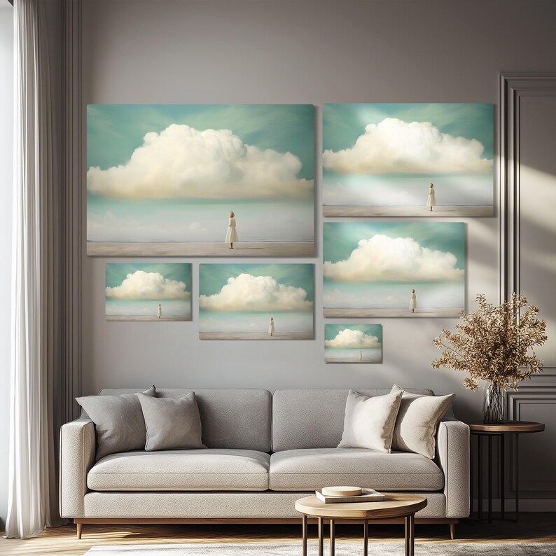 May include: A collection of five framed prints featuring a woman standing on a beach with a large cloud in the sky. The prints are arranged in a grid pattern on a wall above a gray sofa.