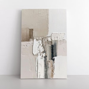 May include: Abstract art canvas with a textured, layered design. The artwork features a palette of neutral tones, including beige, white, and brown, with a mix of brushstrokes and raised areas. The canvas is rectangular and stands upright.