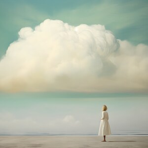 May include: A woman in a white dress stands on a sandy beach, looking out at a large, fluffy white cloud in a blue sky.