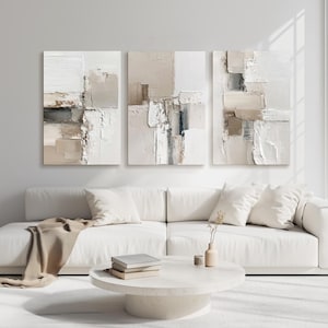 Neutral beige abstract wall art set of three above white sofa in a modern, brightly lit contemporary living room inspiring calmness