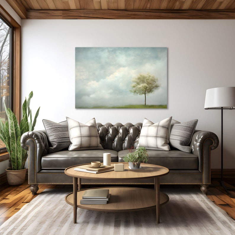 Pode incluir: Um interior de sala de estar com um sof&aacute; de couro marrom, duas almofadas, uma mesa de centro, uma planta em vaso e uma impress&atilde;o emoldurada de uma &uacute;nica &aacute;rvore em um campo com um c&eacute;u nublado.