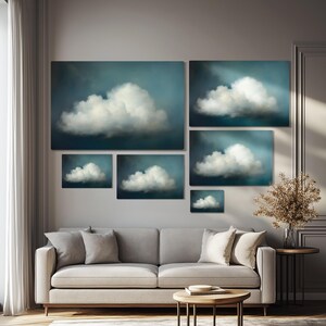 Puede incluir: Un conjunto de seis impresiones de arte de pared abstractas que presentan varios tama&ntilde;os de nubes blancas sobre un fondo azul. Las impresiones est&aacute;n dispuestas en un patr&oacute;n escalonado en una pared sobre un sof&aacute; gris.