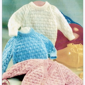 Puede incluir: Imagen de tres suéteres de punto en crema, azul y rosa. El suéter crema es de cuello redondo con un patrón texturizado. El suéter azul tiene un patrón similar y cuello redondo. El suéter rosa es una rebeca con botones. La imagen incluye el texto "waterwheel Double Knitting".