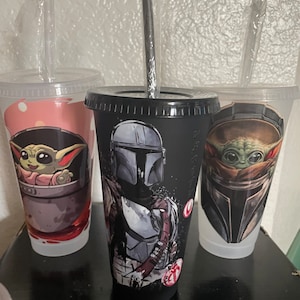 May include: Three reusable cups with black lids and clear straws. The cups feature different Star Wars characters: The Mandalorian, Baby Yoda, and a close-up of Baby Yoda's face.
