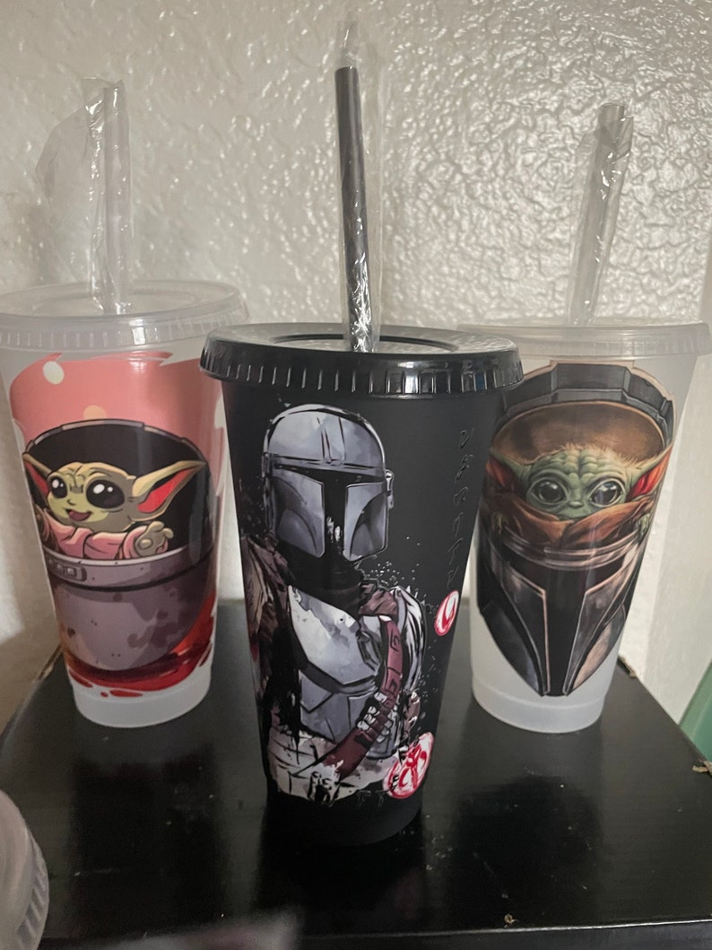 May include: Three reusable cups with black lids and clear straws. The cups feature different Star Wars characters: The Mandalorian, Baby Yoda, and a close-up of Baby Yoda's face.