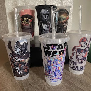 May include: Five clear plastic tumblers with different Star Wars character designs. The designs include The Mandalorian, Baby Yoda, and a group of Star Wars characters. Each tumbler has a clear plastic straw.