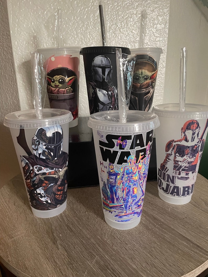 May include: Five clear plastic tumblers with different Star Wars character designs. The designs include The Mandalorian, Baby Yoda, and a group of Star Wars characters. Each tumbler has a clear plastic straw.