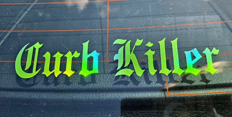 May include: A vinyl decal sticker applied to a dark glass surface featuring the text Curb Killer in a stylized gothic font. The lettering displays a vibrant gradient color transition shifting from bright lime green to a deep cyan blue hue.