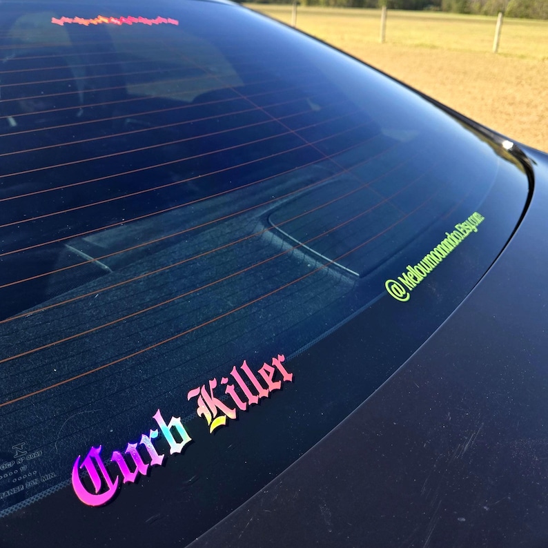 May include: A car window decal featuring the text Curb Killer in a gradient rainbow font with a gothic typeface. A smaller lime green decal with the text @mellowmoonandco.etsy.com is positioned along the right edge of the rear windshield.