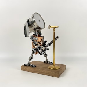Könnte beinhalten: Ein silberner Roboterhund, der eine elektrische Gitarre mit einem Mikrofonständer spielt. Der Roboterhund ist aus Metall und hat einen kupfernen Körper. Die Gitarre ist schwarz und hat ein weißes Schlagbrett. Der Mikrofonständer ist golden.