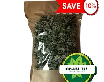 Op de afbeelding: Een bruine papieren zak met een doorzichtig plastic venster, gevuld met gedroogde groene bladeren. De zak heeft een label met de tekst "100% NATUTRAL ORGANIC PRODUCT" en een groen bladerenontwerp. Er is een rood en wit label met de tekst "SAVE 10%".
