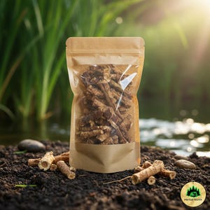 May include: A clear, resealable pouch filled with dried, brown herbal roots. The pouch is made of brown paper with a clear window. Several roots are scattered on the dark soil in front of the pouch. The background features a body of water and green plants.