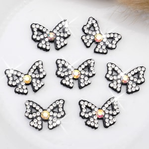May include: Six black fabric bows with rhinestone embellishments. Each bow has a single iridescent rhinestone in the center.