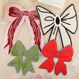 Könnte beinhalten: Vier Filzstoff-Schleifen-Patches in verschiedenen Farben und Stilen. Die Schleifen sind rosa mit rot, weiß mit schwarz, grün mit braun und rot mit weiß.