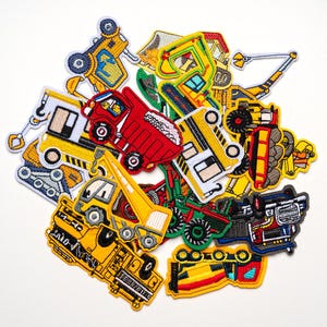 May include: A collection of embroidered patches featuring various construction vehicles. The patches include a red dump truck, yellow excavators, a crane, and other heavy machinery. Each patch has detailed stitching and vibrant colors.