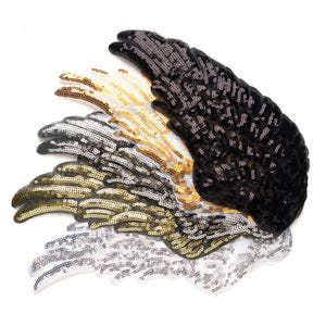 May include: A collection of sequined wing patches in various colors, including black, gold, silver, and white. The patches are arranged in a layered pattern, with each wing displaying a different color and texture. The sequins catch the light, creating a shimmering effect.
