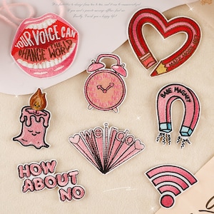 May include: Nine pink and red embroidered iron-on patches with various designs and sayings, including "Your Voice Can Change the World", "We're Weird", "How About No", "Babe Magnet", and "Make More Art".